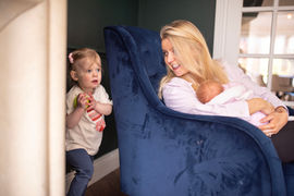 mum holding new born baby girl as older daughter plays around them