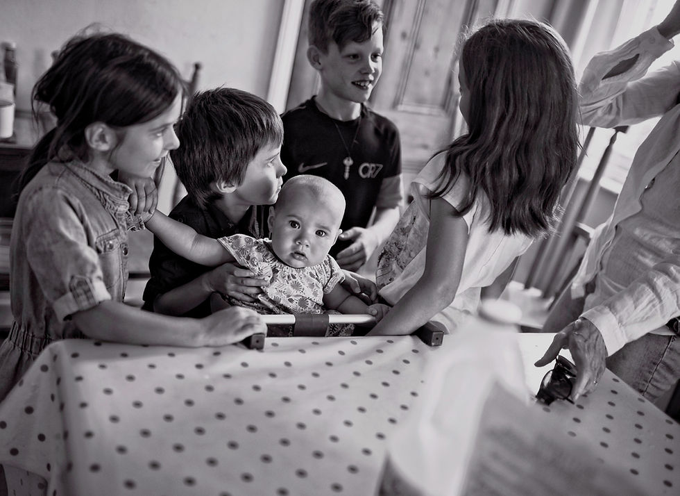 small children gathering around a baby in a high chair at the kitchen table at home