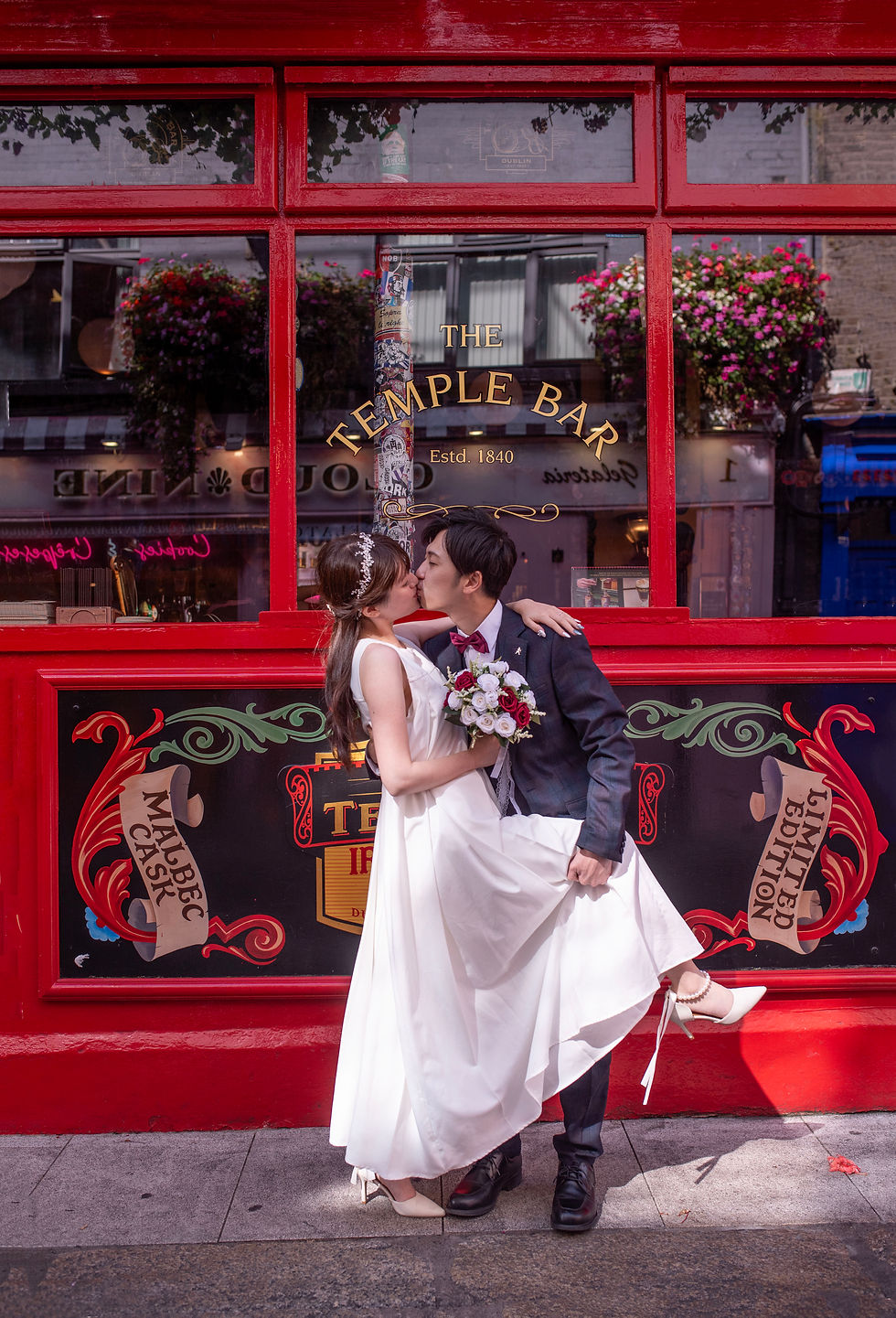 couple kissing romantically outside bright red painted pub in Temple Bar in Dublin - with The Temple Bar written in gold letters on window and town reflected