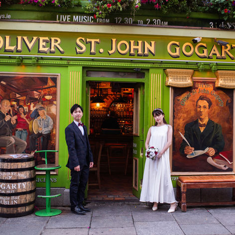 couple standing out brightly painted pub in Temple Bar Dublin either side of doorway with view into golden light of pub