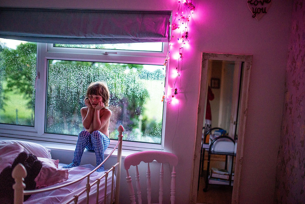 boy sitting on window ledge at home in bedroom with grump face illuminated by pinnk glow in dark lights