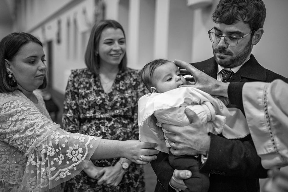 priest blessing baby boy with family surrounding him