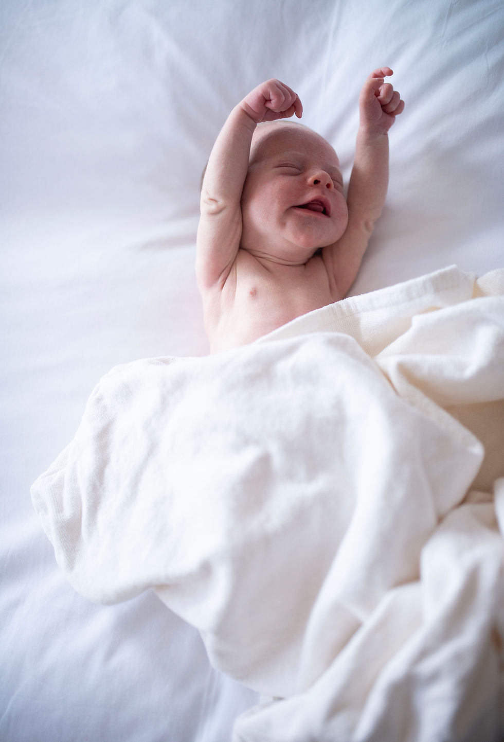 tiny newborn stretching arms under blanket laid on bed. very small newborn baby