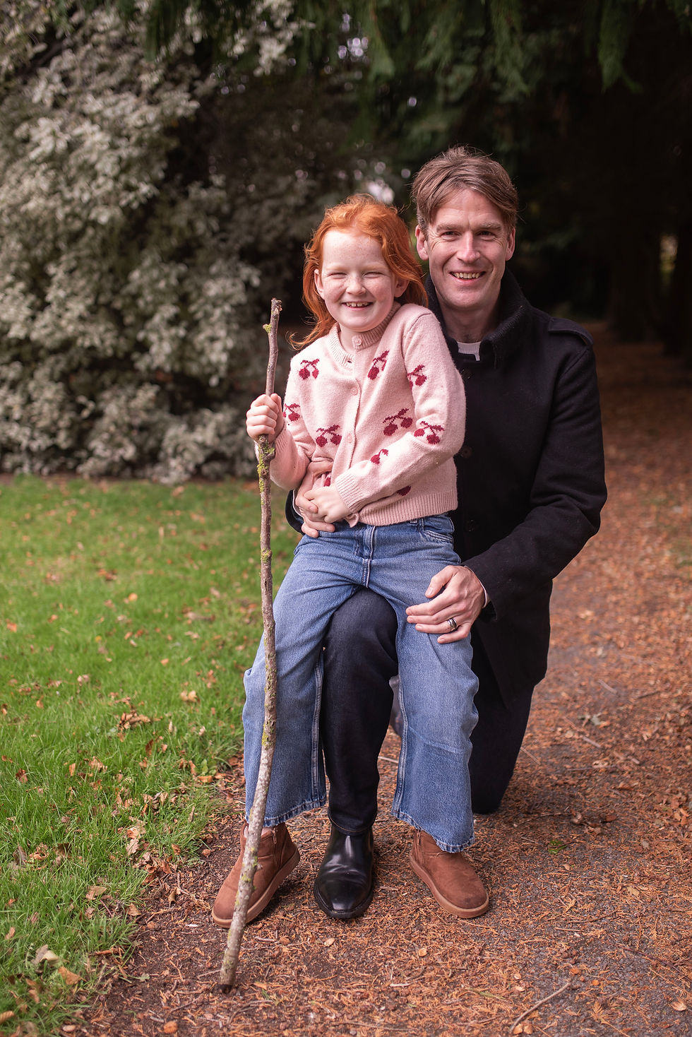 red haired daughter on dad's lap with background of fir trees
