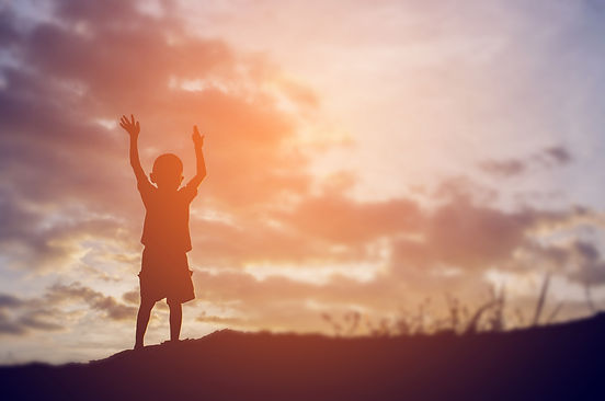 small child with arms raised into the air and a sunset background