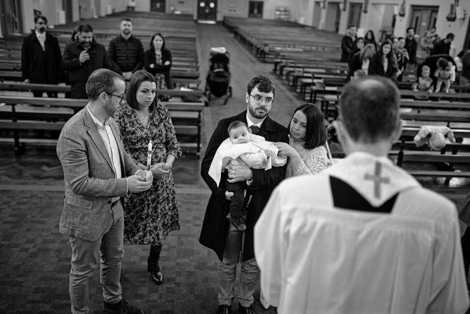 priest reading baptism rites to family, dad holding baby in white blanket at the alter