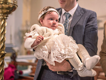 close up detail of baby girls lace christening dress beside large brass candle, held by her dad in her suit