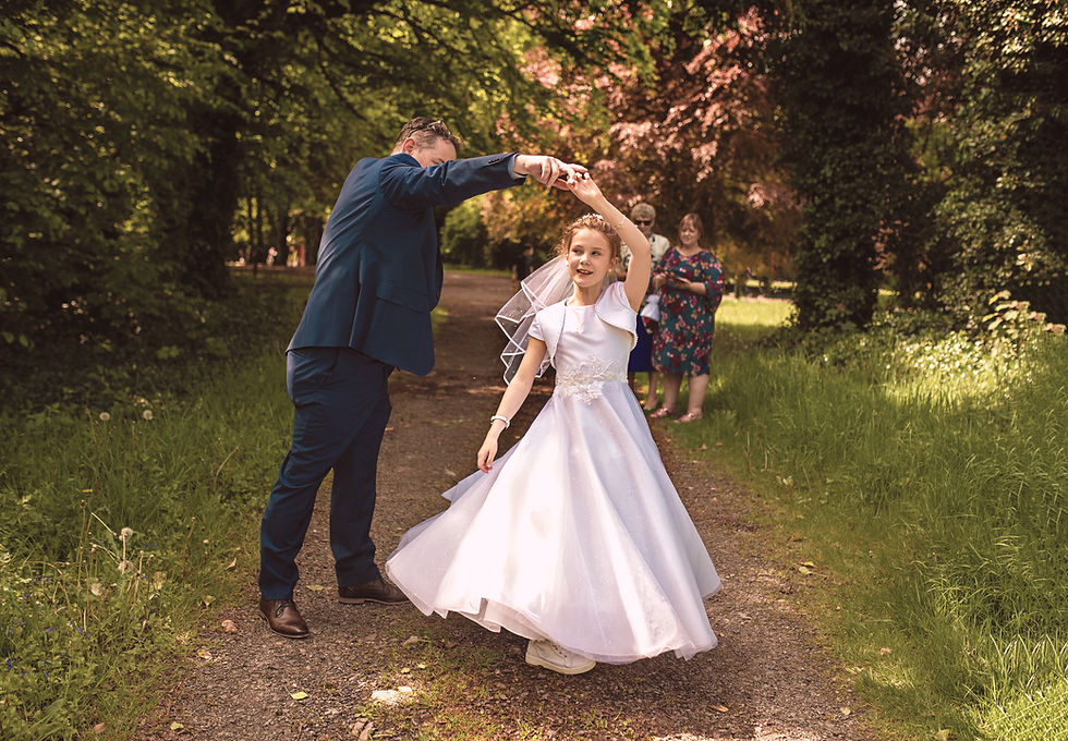 dad spinning his daughter in a white communion dress in dappled summer light