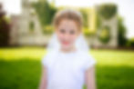 girl in communion dress with headband and veil with castle ruins behind her in soft focus