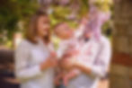 baby reaching out for overhanging lilac blossom as parents smile into intense, patchy dappled summer light. very natural documentary style baby and family portraits all over Dublin
