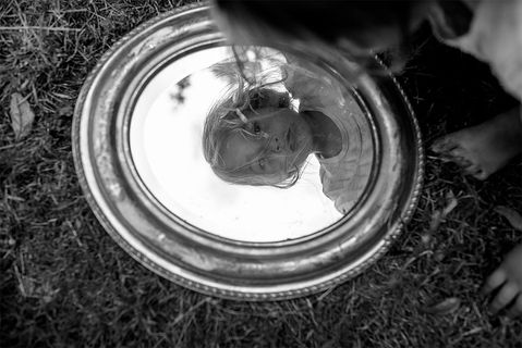 child's reflection in a mirror laid in the grass. at home in the garden. summer family photography photo shoot dublin.