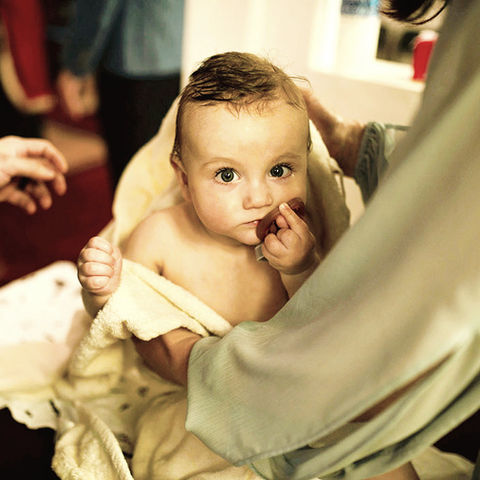 little baby boy swaddled in clothes and towel after baptism in greek orthodox church