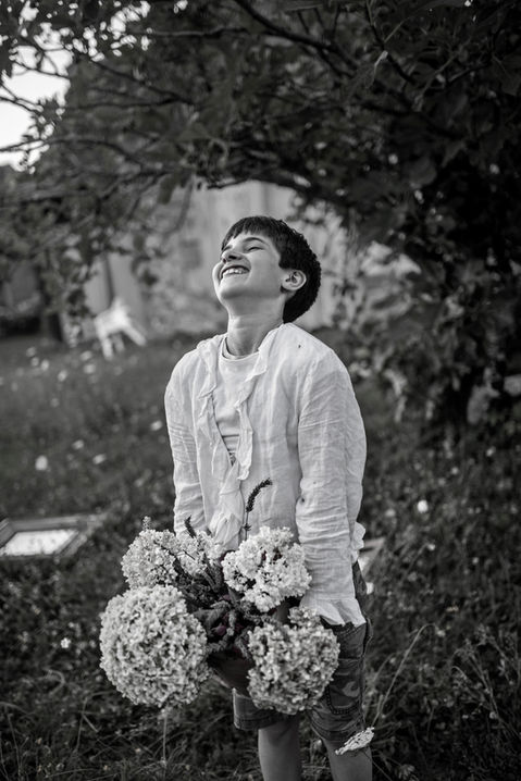 boy with raised face laughing, holding bougainvillea in a garden