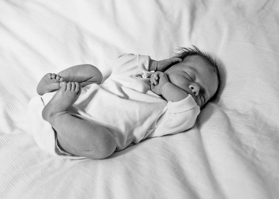 newborn baby close up with hands hed to face - lying on bed at home
