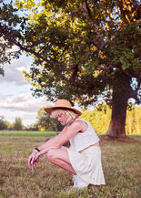 girl in beautiful summer white clothes and hat kneeling under a tree
