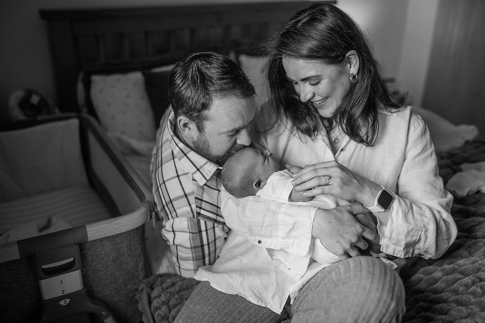 mum and dad on bed kissing baby in their arms at home in the bedroom