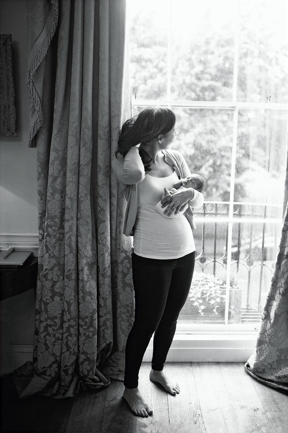 newborn at home session dublin with mum holding newborn naturally by the window, beuatiful window light