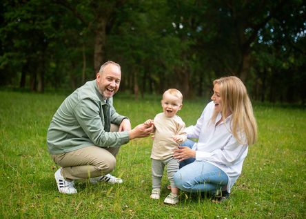 baby boy toddling between mum and dad, in a meadow in Phoenix Park