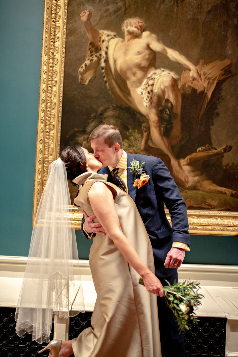 lean and tilt of bride and groom as they kiss in front of old painting