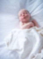 newborn sleeping on master bed wrapped in white blanket