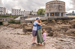 mum and dad hugging with daughter playing by rocks near martello tower on beach