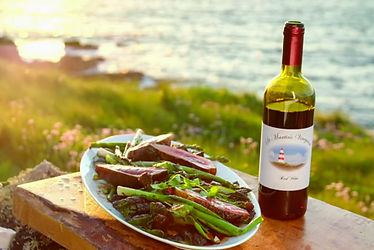A bottle of St Martin's wine beside a plate of freshly cooked food with the sea and coastal vegetation in the background