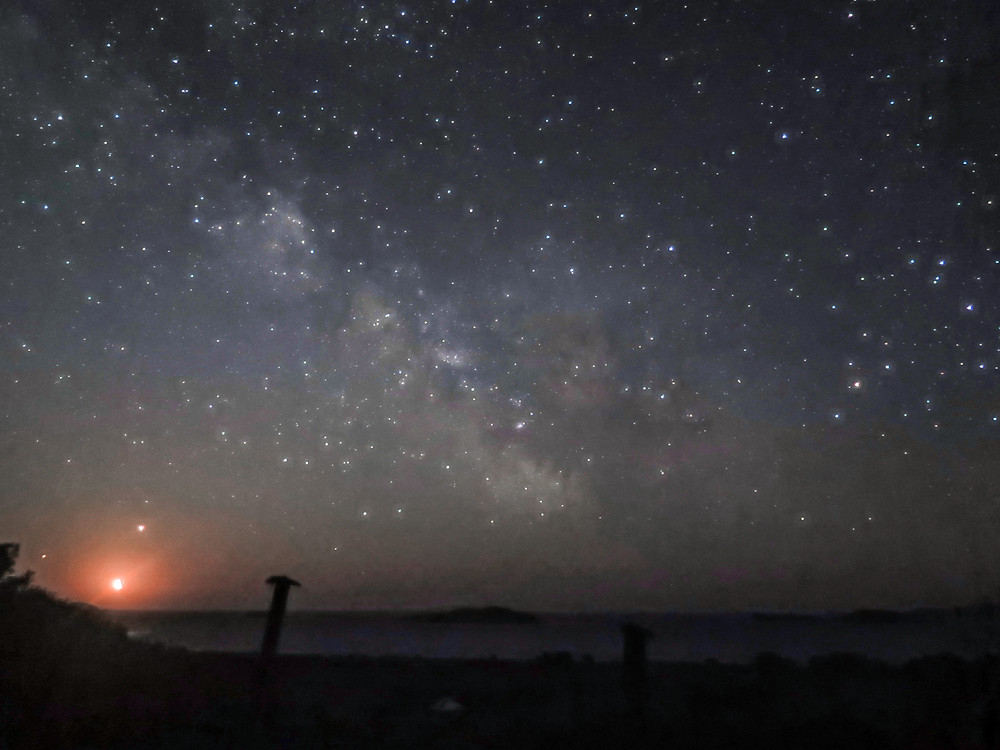 A dark starry sky with the milky way visible - below is the sea with island just discernable