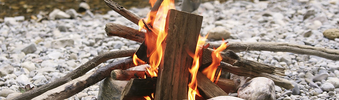 A campfire burns on rocks next to a creek.