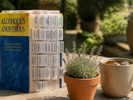 Tabbed AA Big Book on a garden table with a pot of lavender and a cup of tea