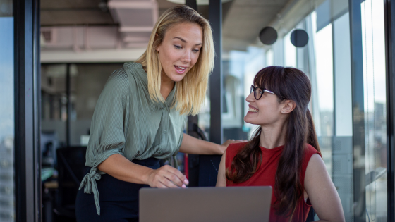 Two business professionals discussing Power Apps while looking at a laptop.
