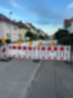 Straßensperre mit Warnleuchten, Stadt im Hintergrund, während Straßenbauarbeiten stattfinden.