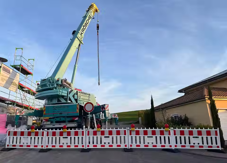 Großer mobiler Kran der Firma Krösche hinter einer aufgestellten Absperrung auf einer Einfahrt, mit blauem Himmel im Hintergrund.