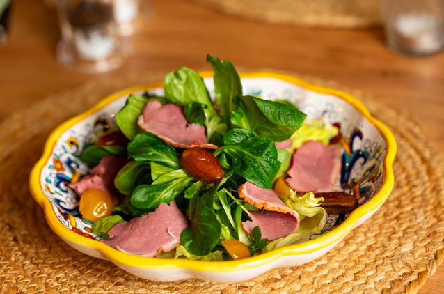 Frischer Salat mit Schinken, Tomaten und einem stilvollen, handbemalten Teller.