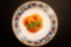 Nahaufnahme von Spaghetti mit Tomatensoße und Basilikum auf einem farbenfrohen Teller vor dunklem Hintergrund.
