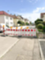 Straßensperre mit Warnleuchten, Baustelle, rote und weiße Barriere, Wohngebiet im Hintergrund.