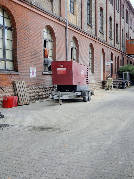 Roter Stromgenerator auf Anhänger vor Backsteingebäude