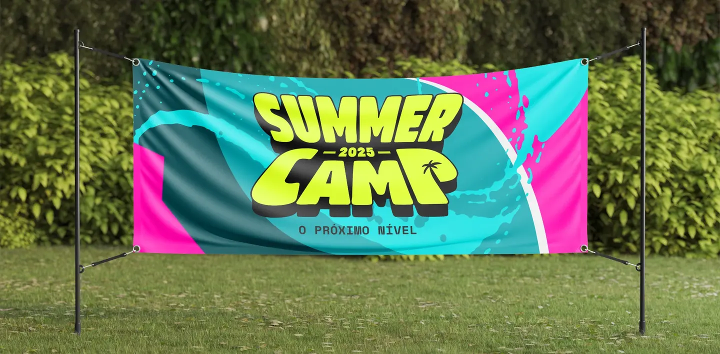 Faixa retangular com arte gráfica em azul e rosa neon, e o logo Summer Camp centralizado, estendida em estrutura metálica sobre gramado com árvores ao fundo.