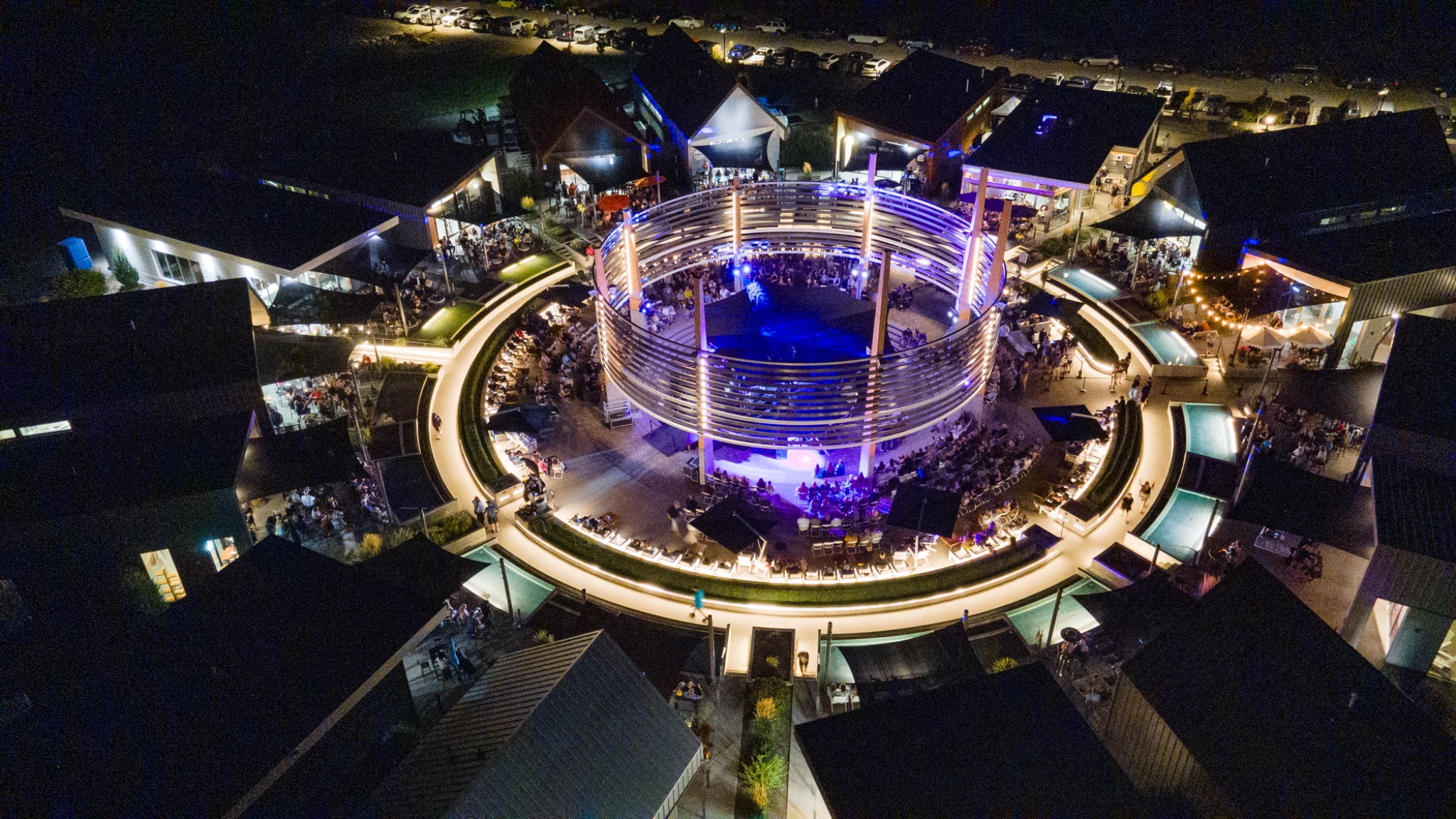 Aerial night photograph of a circular outdoor event stage and illuminated venue with a crowd and purple-blue concert lighting in Oliver, BC