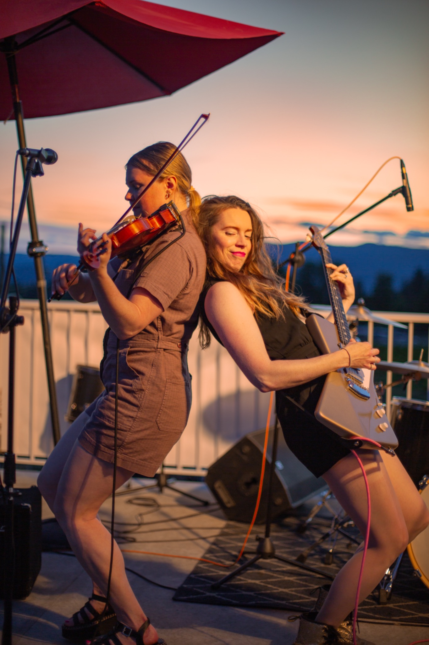 Violinist and guitarist performing back to back on an outdoor stage during sunset in the Okanagan, British Columbia