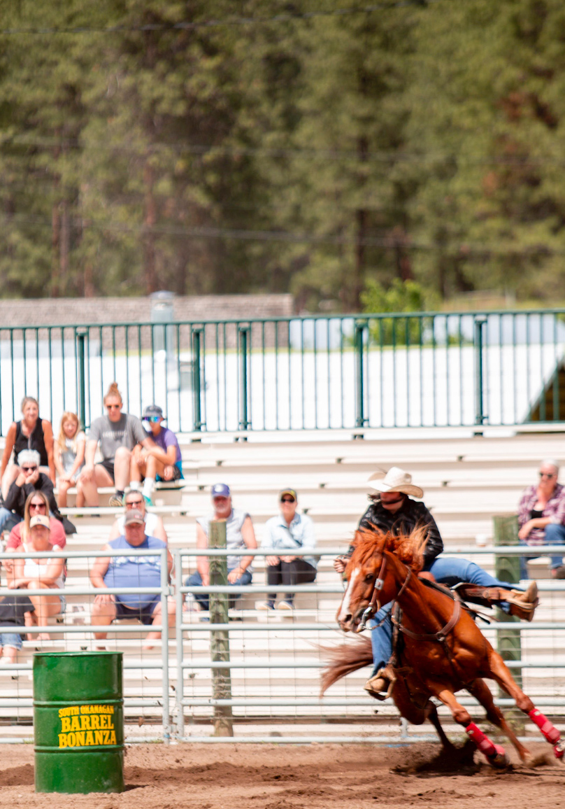 Cowboy in a dark shirt and white hat rounding a barrel at the South Okanagan Barrel Bonanza equestrian event
