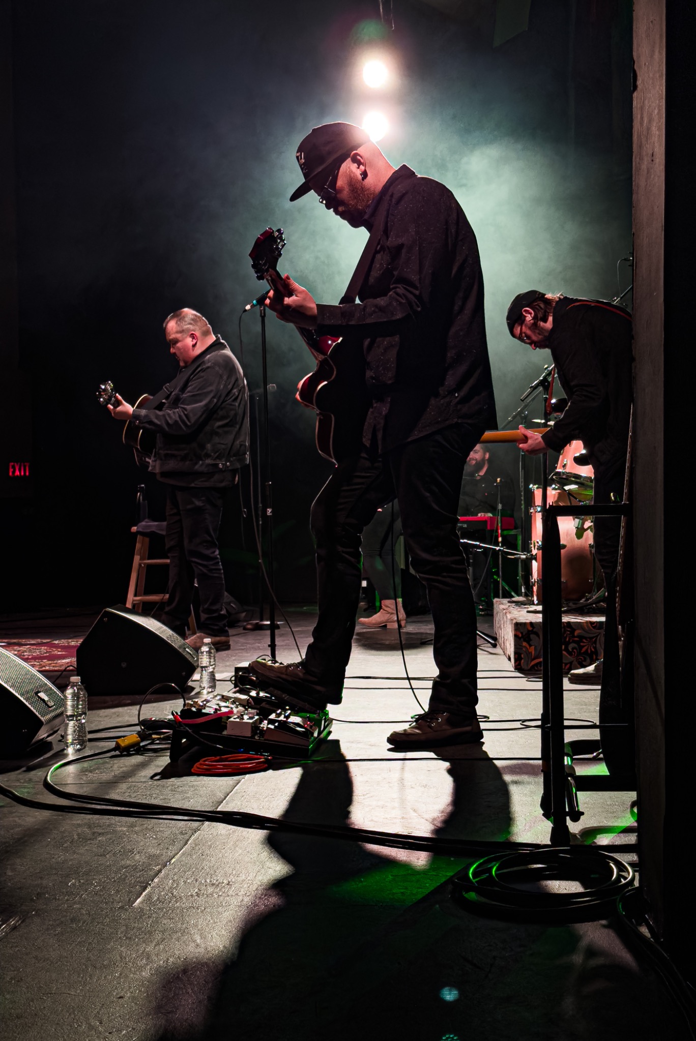 Three guitarists playing on a dim concert stage with a spotlight, coloured lighting and atmospheric smoke