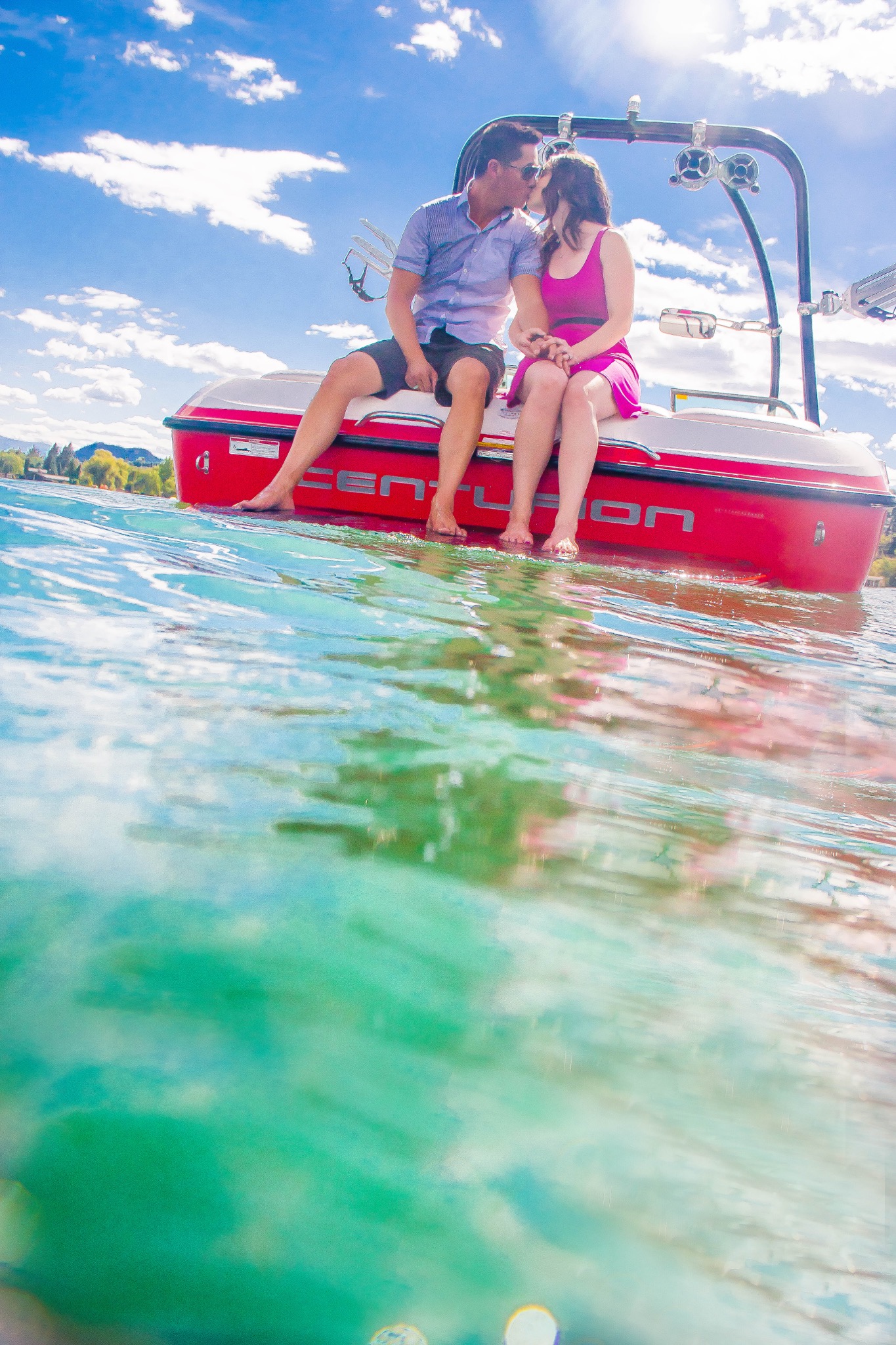 Couple sharing an intimate moment while seated on the side of a red boat on a lake