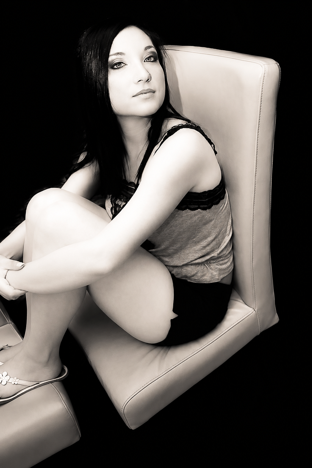 Black-and-white studio portrait of a dark-haired woman seated in a high-backed chair against a dark backdrop