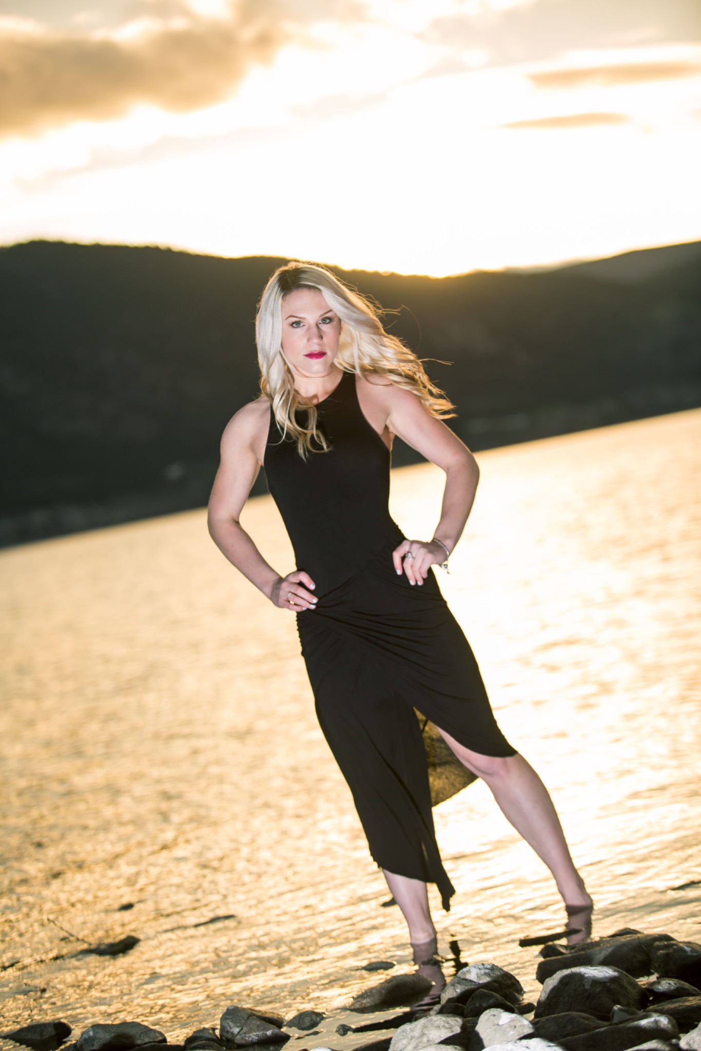 Golden-hour editorial portrait of a woman in a black dress standing by the water