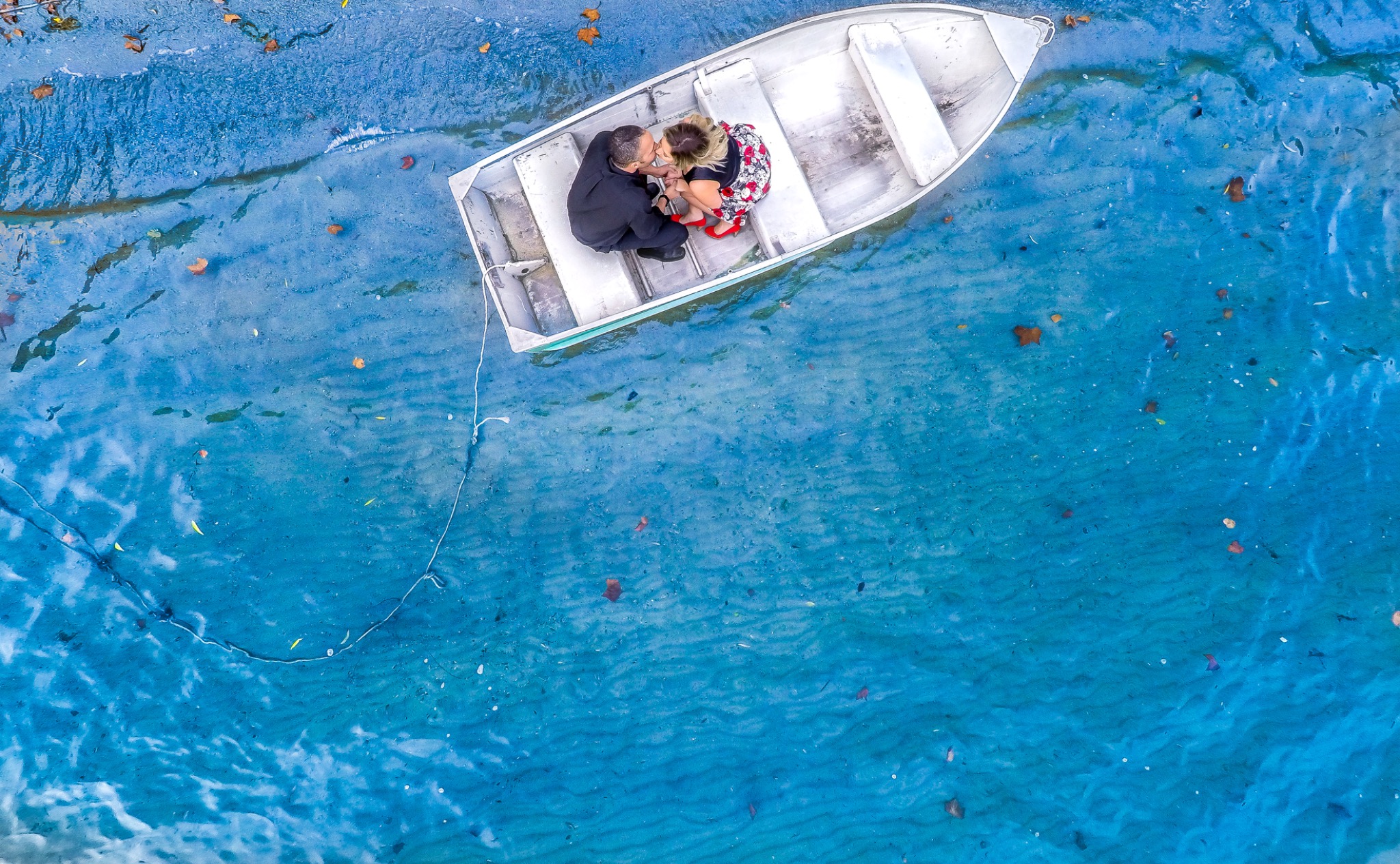 Aerial photograph of a couple sharing a quiet moment in a small boat on blue water