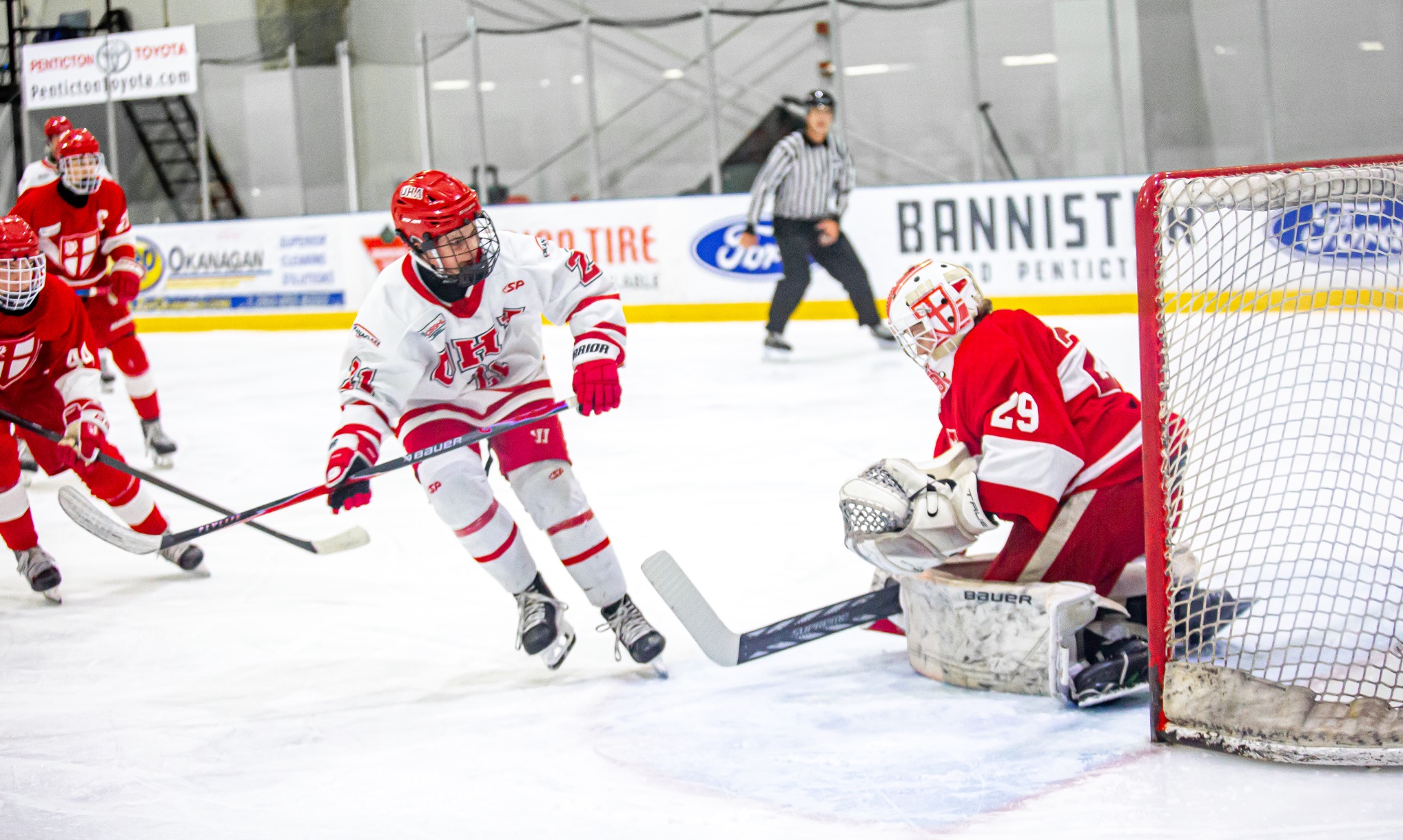 Youth ice hockey player attacking the goal as a goalie in a red jersey makes a save during a hockey game at a Penticton rink