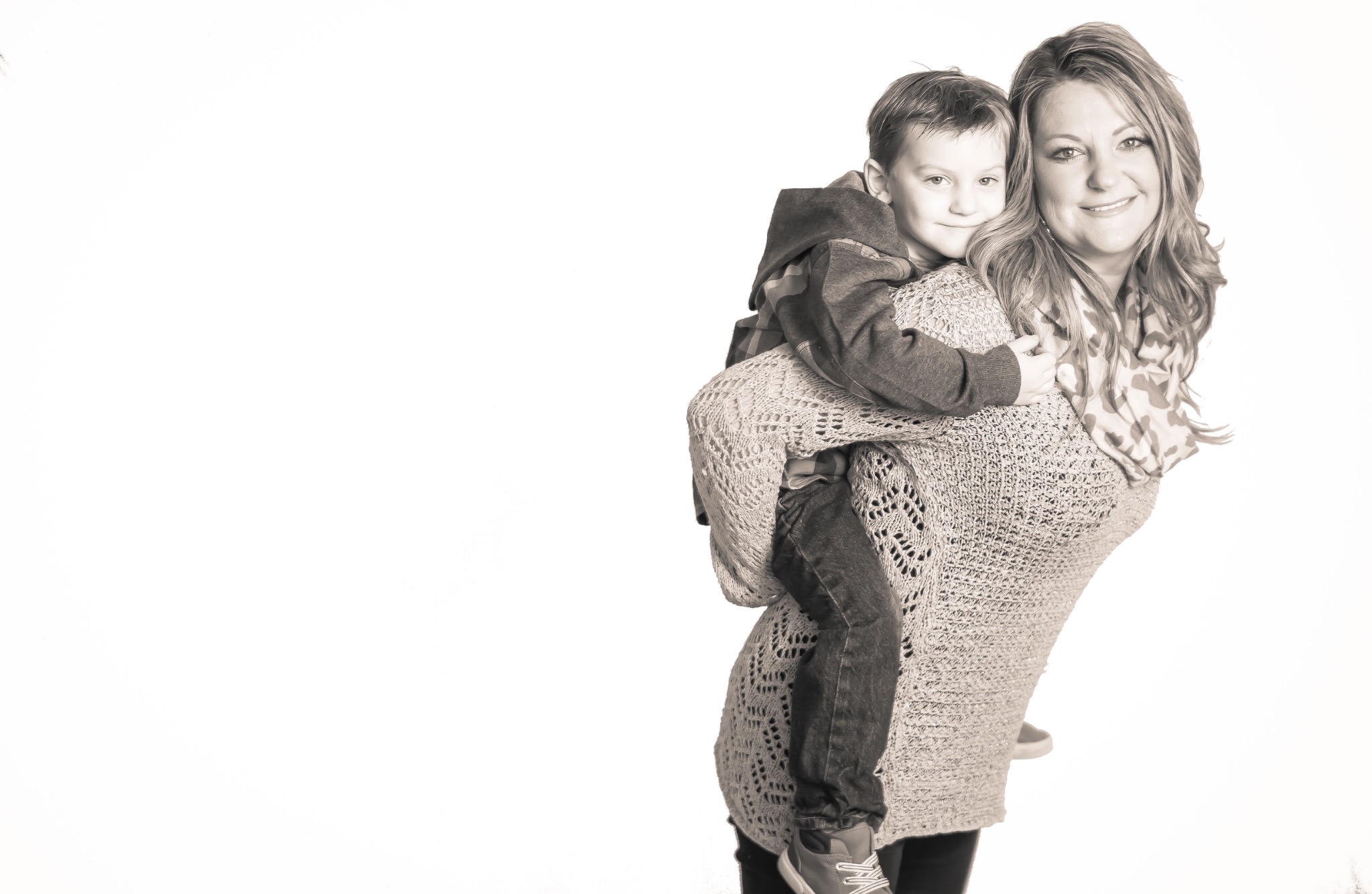 Black-and-white portrait of a mother carrying her smiling young son against a bright studio background
