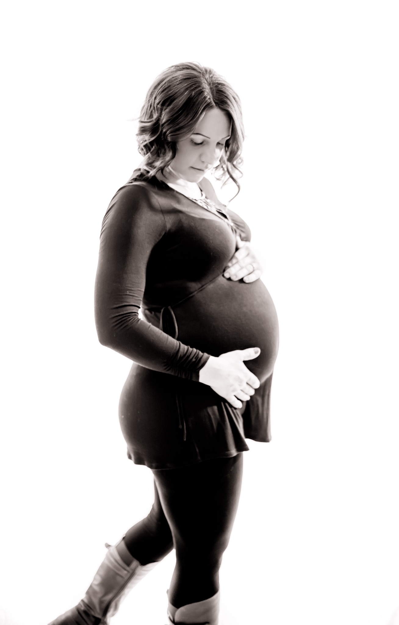 Black-and-white maternity portrait of an expectant mother against a light studio backdrop