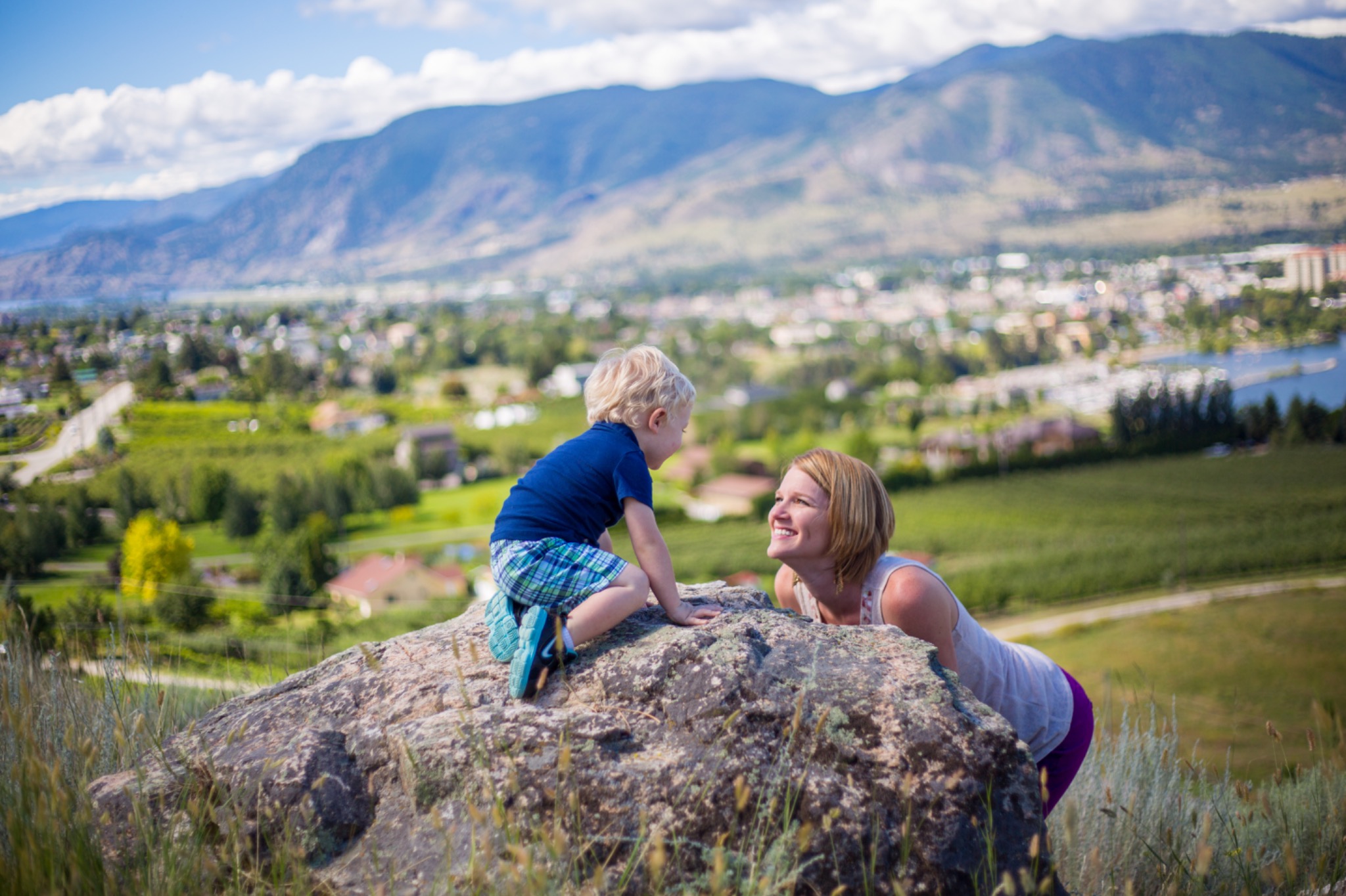 Mother and young child smiling together beside a rock with Okanagan hills behind