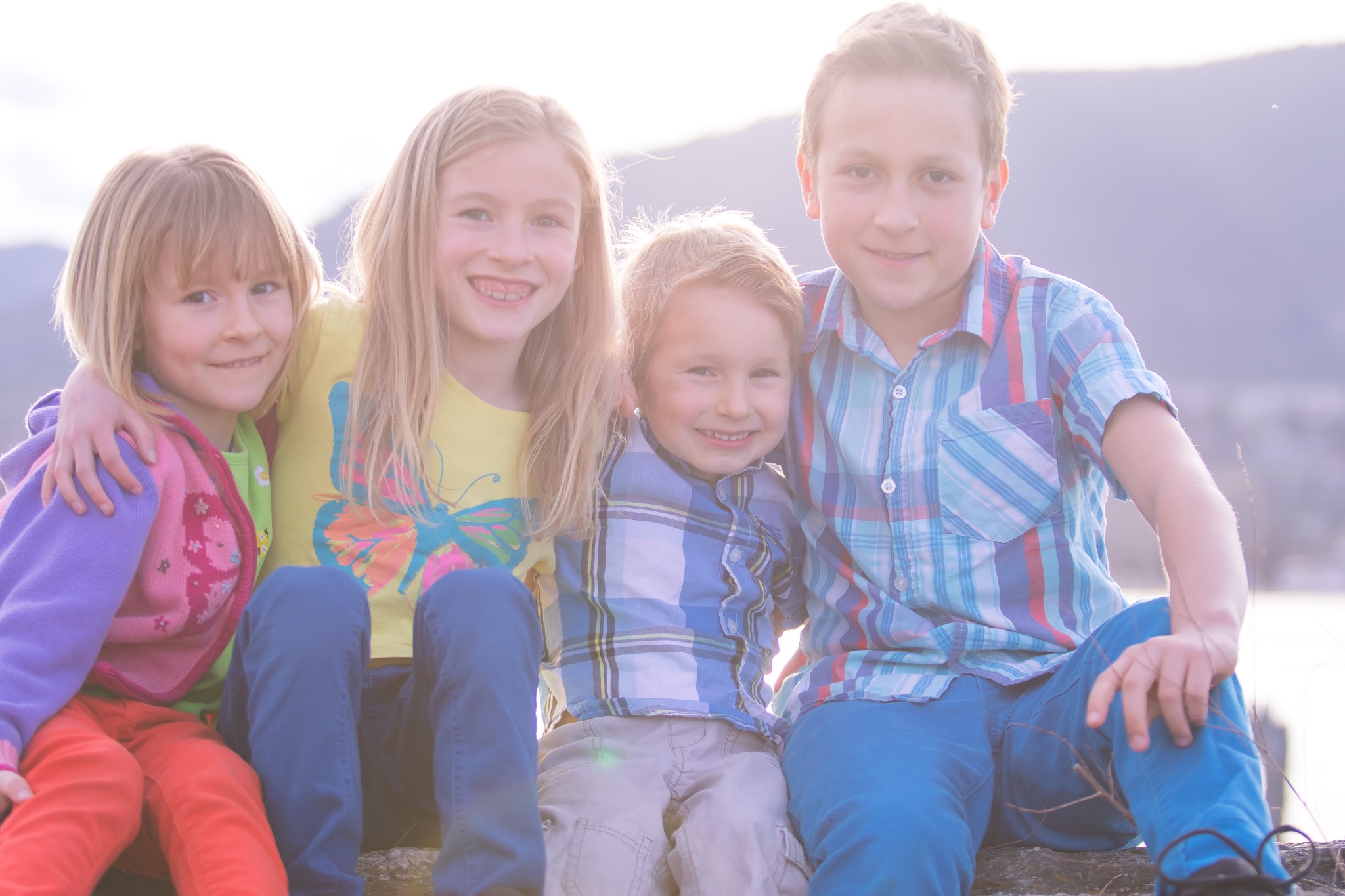 Four children smiling together in a sunlit outdoor family portrait